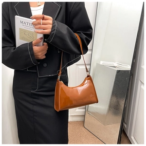 Détail d'un sac baguette en cuir verni marron porté avec un blazer noir élégant