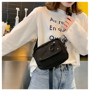 Detail view of a black canvas crossbody bag worn over a white T-shirt in a cafe setting