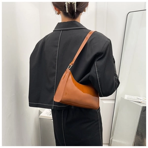 Détail d'un sac à épaule en cuir verni brillant de couleur caramel porté par un mannequin