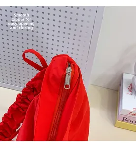 Close-up of smooth silver zipper and pleated nylon strap on a red crossbody bag
