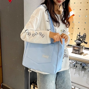 Detail of light blue nylon tote bag with front pocket and white fashion label