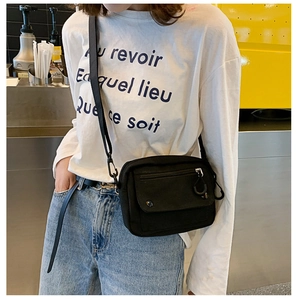 Detail of a black canvas crossbody bag with a front zipper and stylish flap closure design