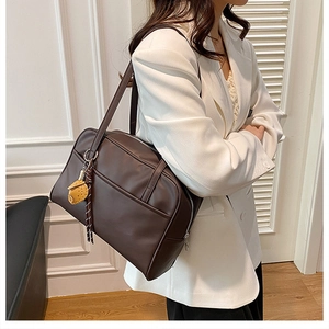 Detailed side view of dark brown leather shoulder bag with a yellow pendant charm