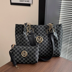 Detail of black tote bag set with monogram M pattern and gold chain hardware accents