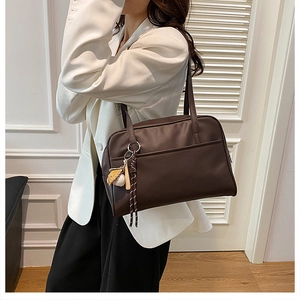 Detail of deep brown shoulder tote bag with zipper closure and stylish baseball charm