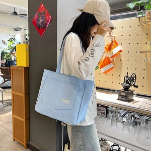 Close-up detail of light blue nylon tote bag featuring front pocket and fashion label