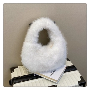 Détail d'un sac hobo blanc en fausse fourrure pelucheuse posé sur une valise blanche
