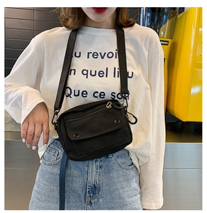 Detail of black canvas crossbody bag showing durable wide shoulder strap and metal hardware