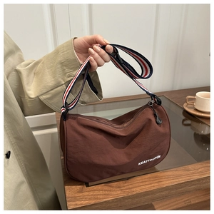 Dettaglio borsa a mezzaluna marrone in nylon con tracolla tricolore e logo KEAIYOUPIN su legno