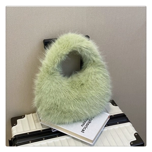 Détail d'un sac à main en peluche vert clair posé sur un livre et une valise