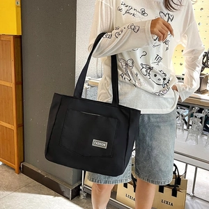 Detail of black nylon tote bag featuring a large front pocket and metal fashion plaque