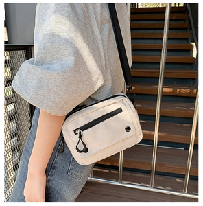 Detail view of cream canvas crossbody bag with adjustable black strap on a model