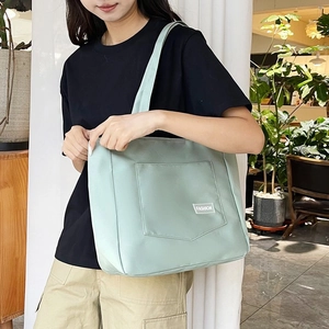 Detail of mint green nylon tote bag featuring front pocket with white Fashion label