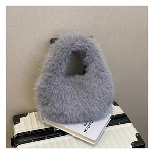 Détail d'un sac à main en fausse fourrure gris clair posé sur une valise avec style