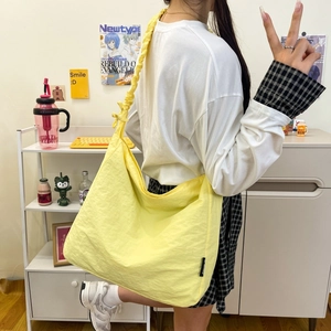 Detail of a bright yellow nylon hobo bag with a pleated strap and ruched texture