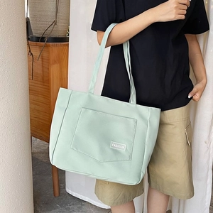 Detail of mint green nylon tote bag featuring a front pocket with a white fashion label