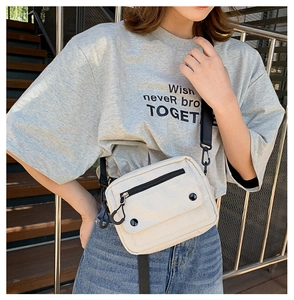 Close-up of minimalist cream canvas crossbody bag with black buckle flap and wide strap