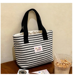 Detail view of large striped canvas tote bag with black handles and rectangular brand label