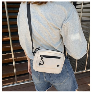 Close-up of minimalist beige canvas crossbody bag with black adjustable strap and flap detail