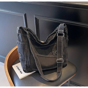 Détail du sac bandoulière en toile noire avec surpiqûres blanches et bords effilochés