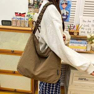 Detail view of dark brown nylon crossbody bag featuring a wide pleated shoulder strap design