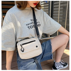 White canvas crossbody bag with adjustable wide black strap shown on a model