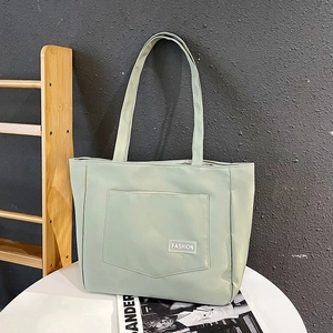 Detail view of large mint green nylon tote bag featuring front pocket and fashion label