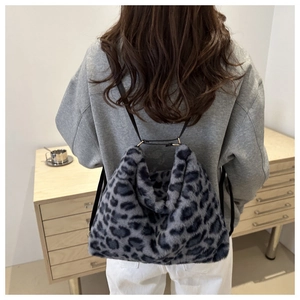 Detail of blue leopard print faux fur backpack shown on a model in a minimalist home setting