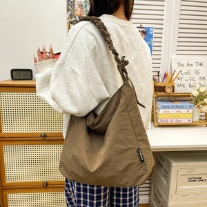 Detail of brown nylon tote bag featuring a ruffled cloud-style drawstring shoulder strap