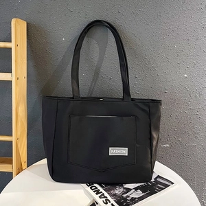 Close-up of a large black nylon tote bag featuring a front pocket and Fashion label
