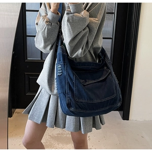 Grand sac à bandoulière en jean bleu foncé porté par un mannequin au style rétro urbain