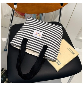 Detail of striped canvas tote bag with woven handles and colorful brand logo patch