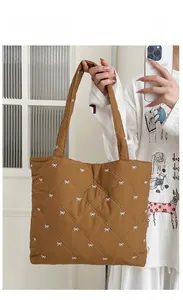 Close-up of brown quilted tote bag featuring white bow embroidery and diamond pattern