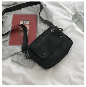 Detail of minimalist black nylon crossbody bag with flap pocket on a white fabric background