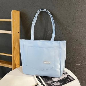 Detail view of light blue nylon tote bag with front pocket and fashion label on table