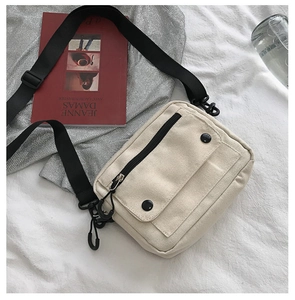 Close-up of beige canvas crossbody bag with large front pocket and black adjustable strap