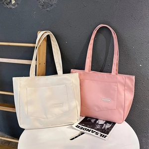 Detail view of cream and pink nylon tote bags with exterior pockets and fashion labels