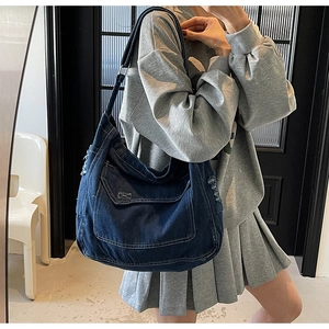 Gros plan sur un sac à bandoulière en denim bleu foncé avec surpiqûres et détails effilochés