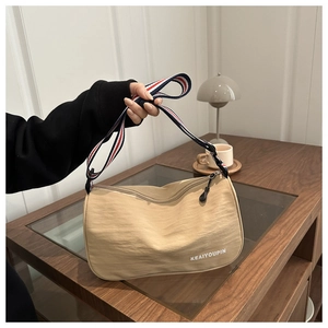 Dettaglio della borsa a tracolla beige in nylon con cinturino a righe sul tavolo