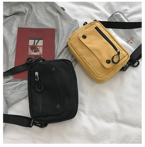 Detail of canvas crossbody bags in black and ginger yellow with front flap pocket and strap