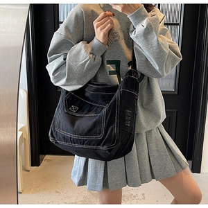 Détail du sac bandoulière en denim noir avec coutures contrastées et grande poche à rabat