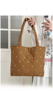Detailed view of brown quilted tote bag with white bow patterns and wide shoulder straps