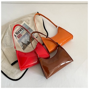 Détail de trois sacs baguette brillants en orange, rouge et café sur un bureau blanc