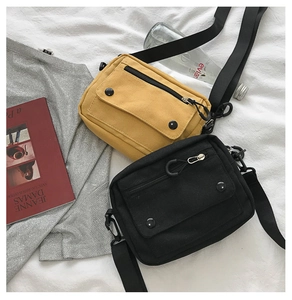 Detail view of canvas crossbody bags in black and yellow with front snap button pocket