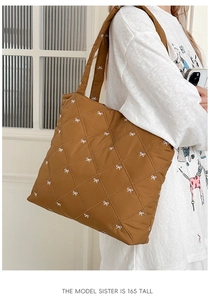 Detail shot of brown quilted tote bag with white bow embroidery and wide shoulder strap