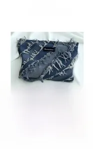 Detail view of denim cosmetic bag showing blue patchwork fabric and frayed fringe trim