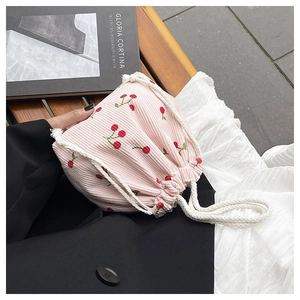 Detail der rosa Cord-Beuteltasche mit Kirschstickerei auf einer Holzbank im Freien