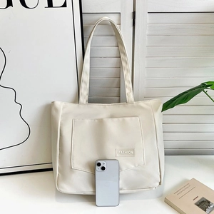 Detail view of a cream nylon tote bag with a front pocket and smartphone for size reference