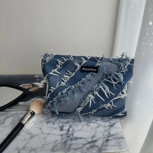 Detail of blue denim cosmetic bag with fringe texture and Moonshine label on marble top