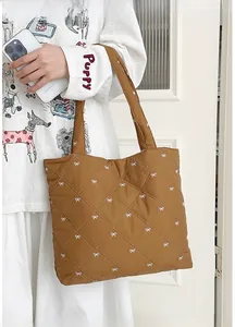 Detail of brown quilted tote bag featuring white bow embroidery and diamond stitching